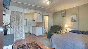 A bedroom with a bed, a chair, a desk, a television, and a bathroom visible through an open door.
