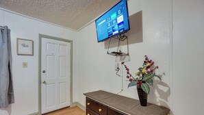 A room with a white door, a flat-screen TV mounted on the wall, a dark wooden dresser with drawers, and a potted plant on the dresser.