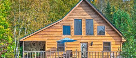A log cabin with a balcony, a dining area, and a view of the surrounding forest.