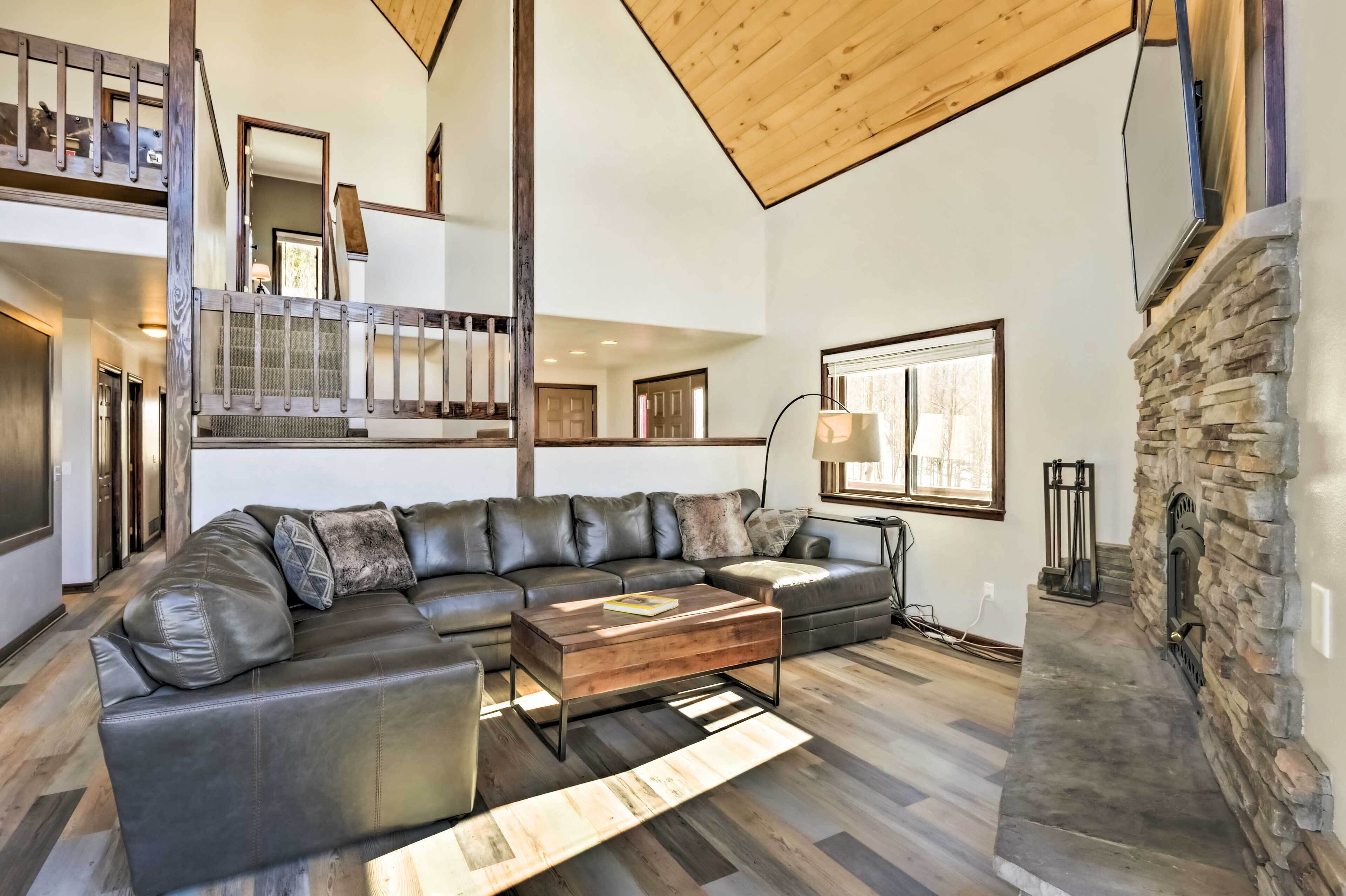 A spacious living room with a large sectional sofa, a wooden coffee table, and a stone fireplace.