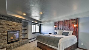 A bedroom with a stone fireplace, a large bed, and a wooden headboard. - Spacious Fairplay Cabin w/ Views ~ 21 Mi to Breck! (Alma)