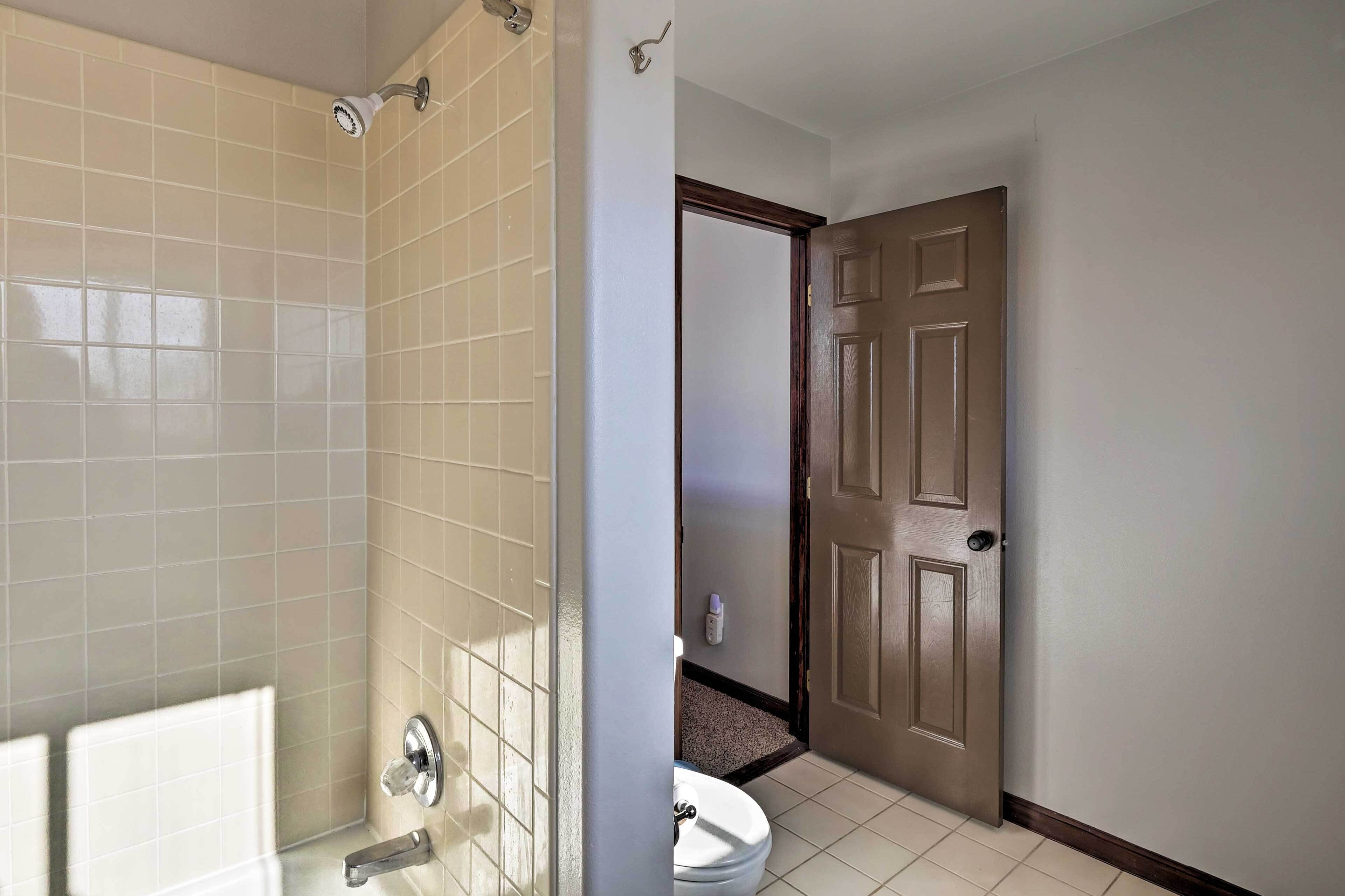 A bathroom with a shower, toilet, and a door leading to another room.