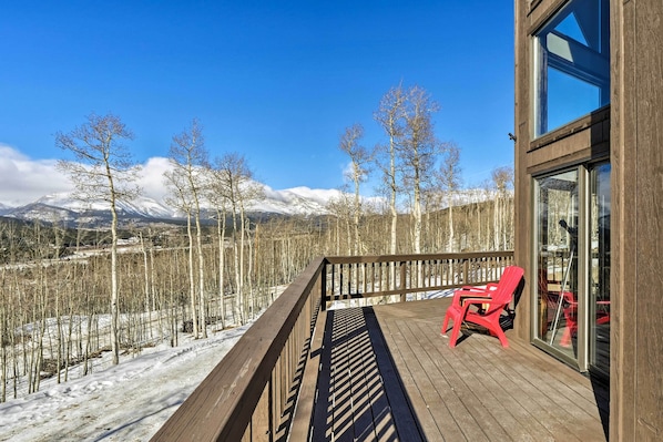 Una terraza de madera con una silla roja, con vistas a un paisaje nevado con árboles y montañas.