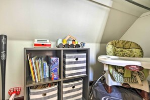A room with a bookshelf containing books and a toy train, a stroller, and a baby carrier.