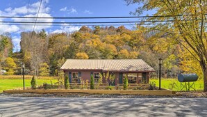 A small building with a red roof and a porch, surrounded by trees and a grassy area. - Colorful Bakersville Cottage: Views, Pets Allowed! (Bakersville)