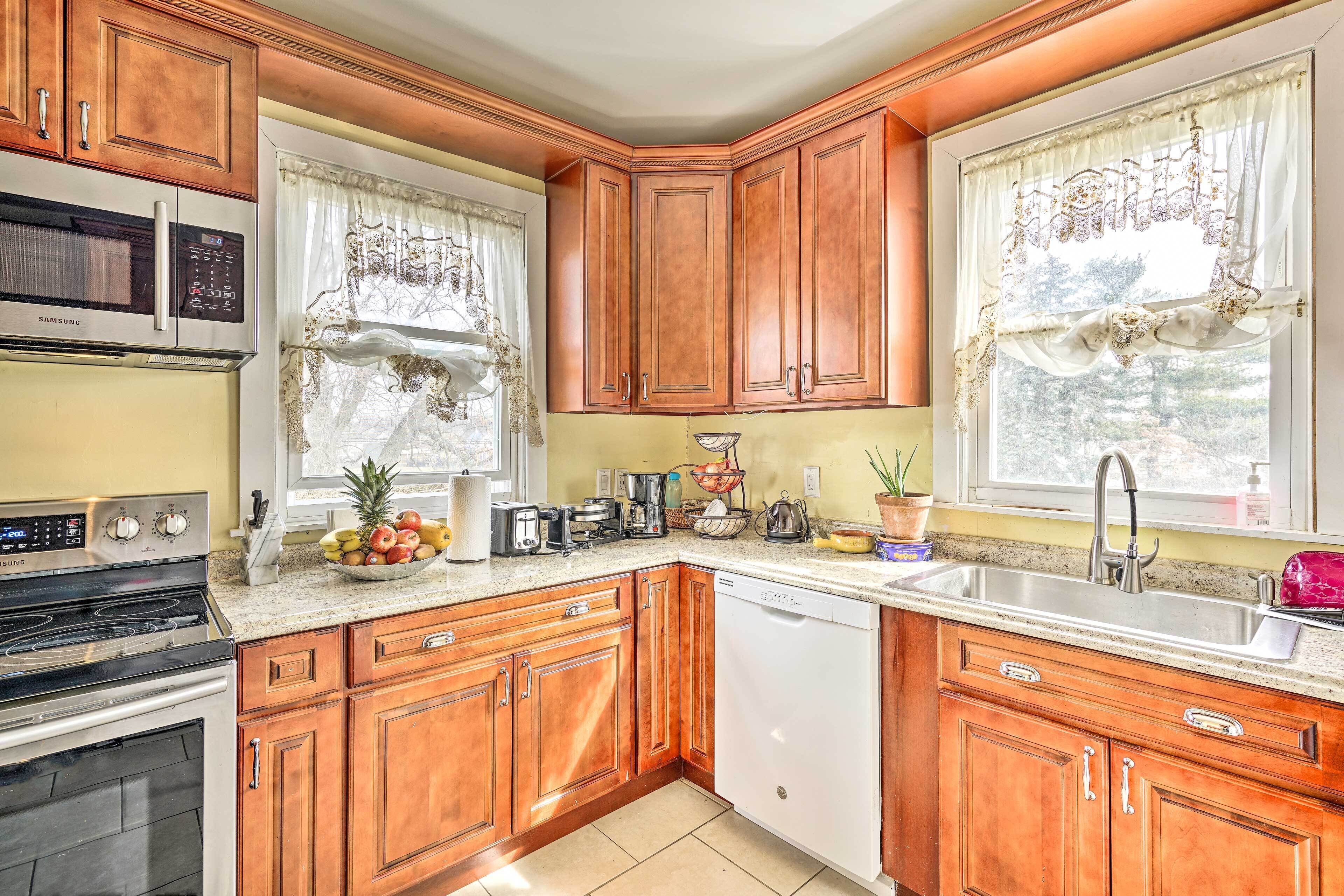 A kitchen with wooden cabinets, a microwave, a stove, a sink, and a window with curtains.