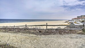 Vista a la playa con un cerco de madera, arena y una hilera de edificios con un paseo curvo.