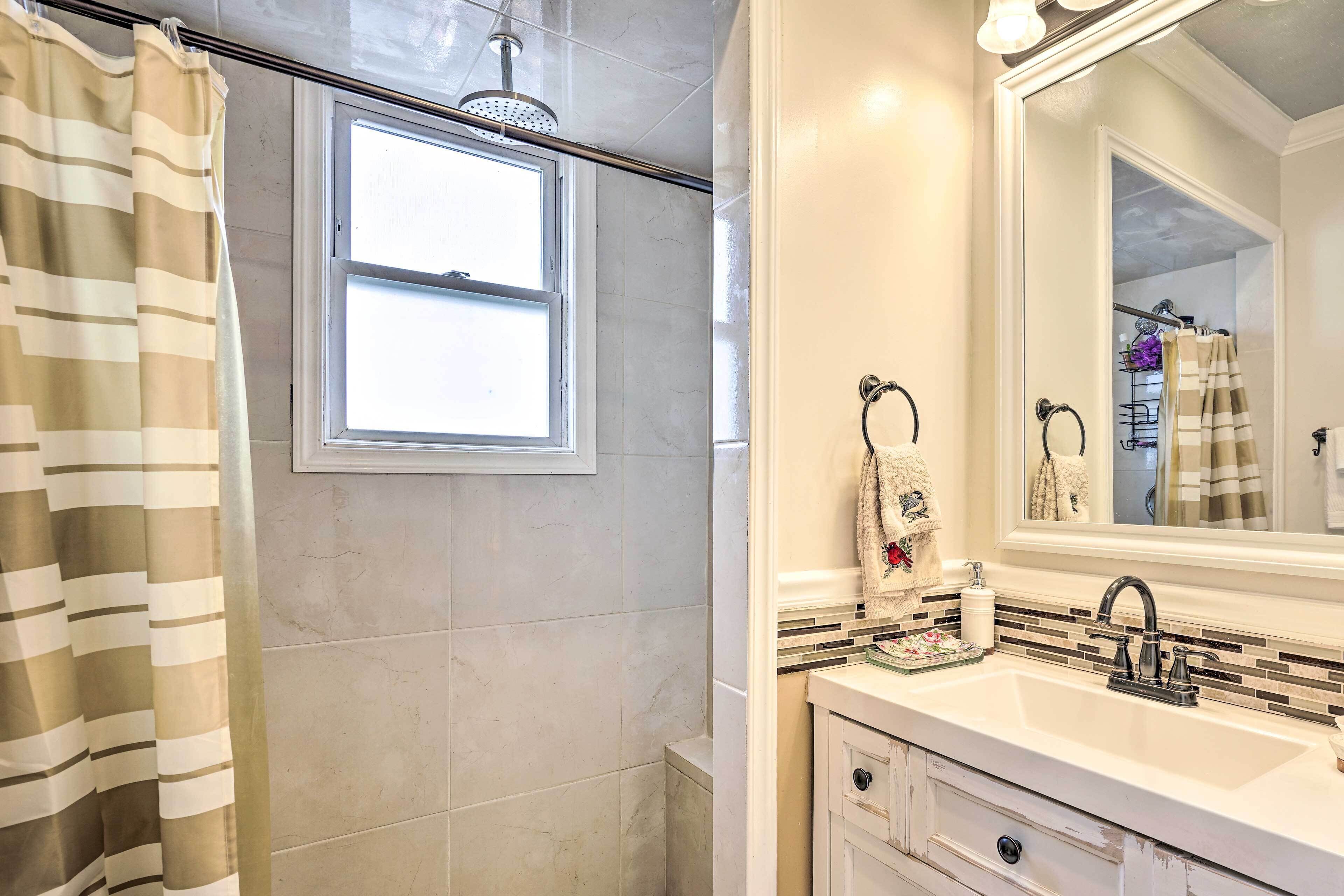 A bathroom with a shower, a window, a sink, and a mirror.