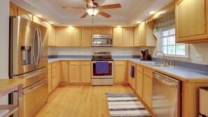A modern kitchen with wooden cabinets, stainless steel appliances, a ceiling fan, and a window with a plaid valance.