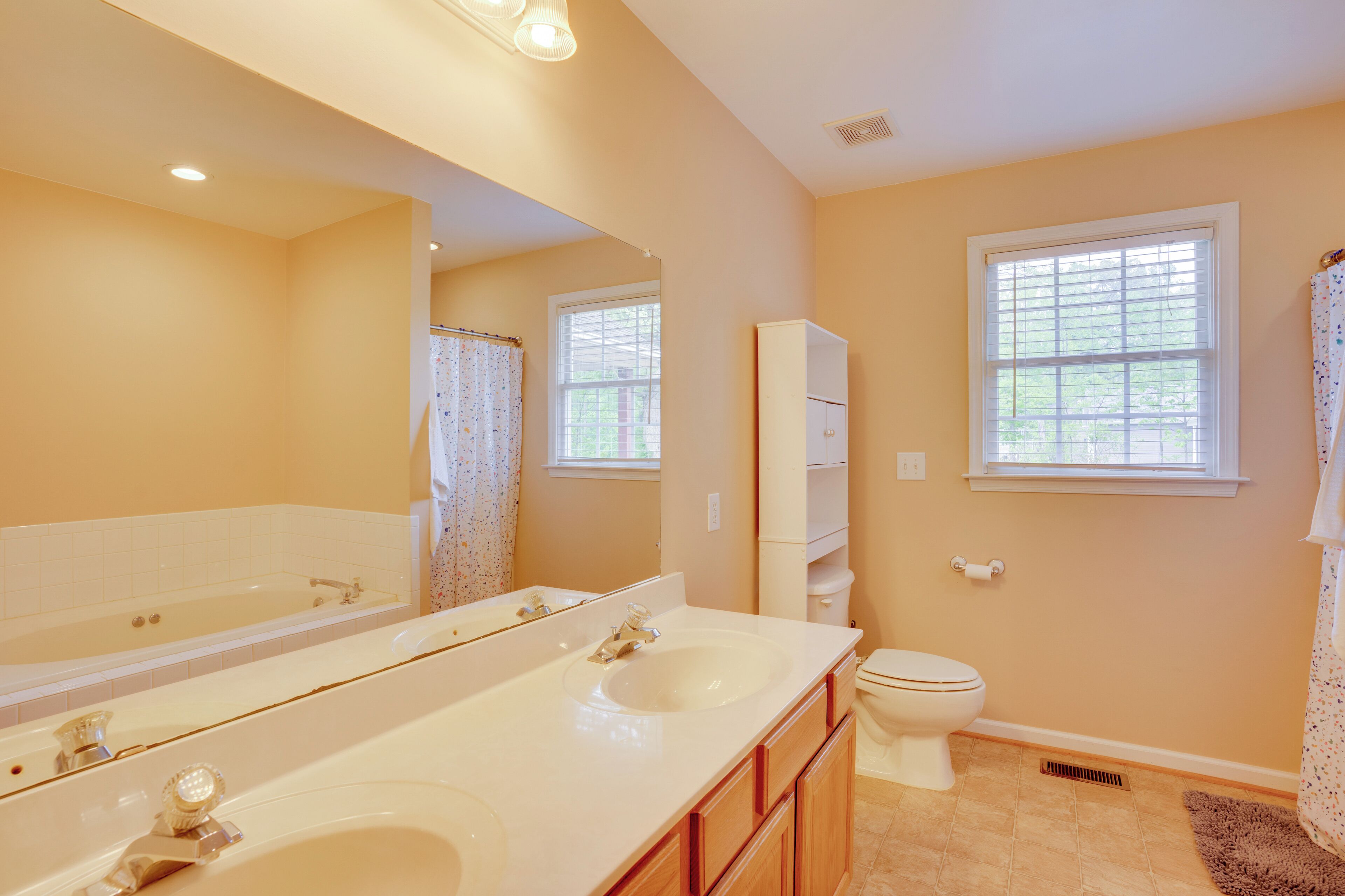 A bathroom with a double sink, a toilet, a bathtub, and a window.