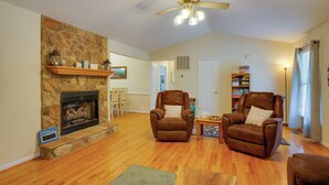 A spacious living room with a stone fireplace, two leather armchairs, a wooden coffee table, and a ceiling fan.