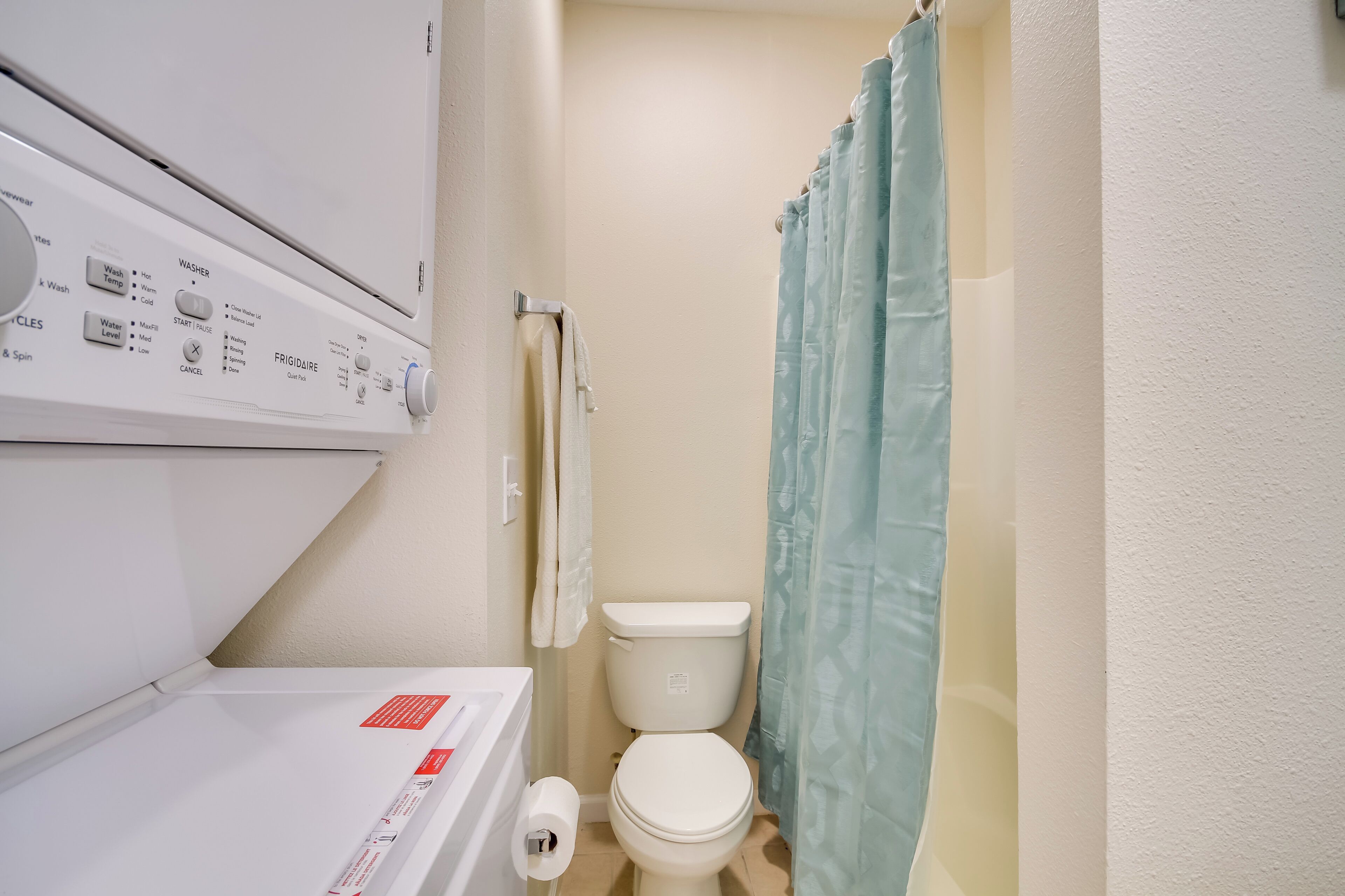 Een kleine badkamer met toilet, handdoekhouder en wasmachine.