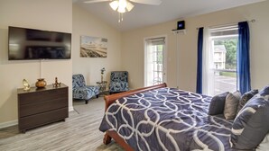Quarto com cama, ventilador de teto, televisão, cômoda, cadeira e janela com cortinas.