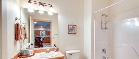 A bathroom with a sink, toilet, and bathtub. There is a towel rack with towels, a mirror, and a sign on the wall.