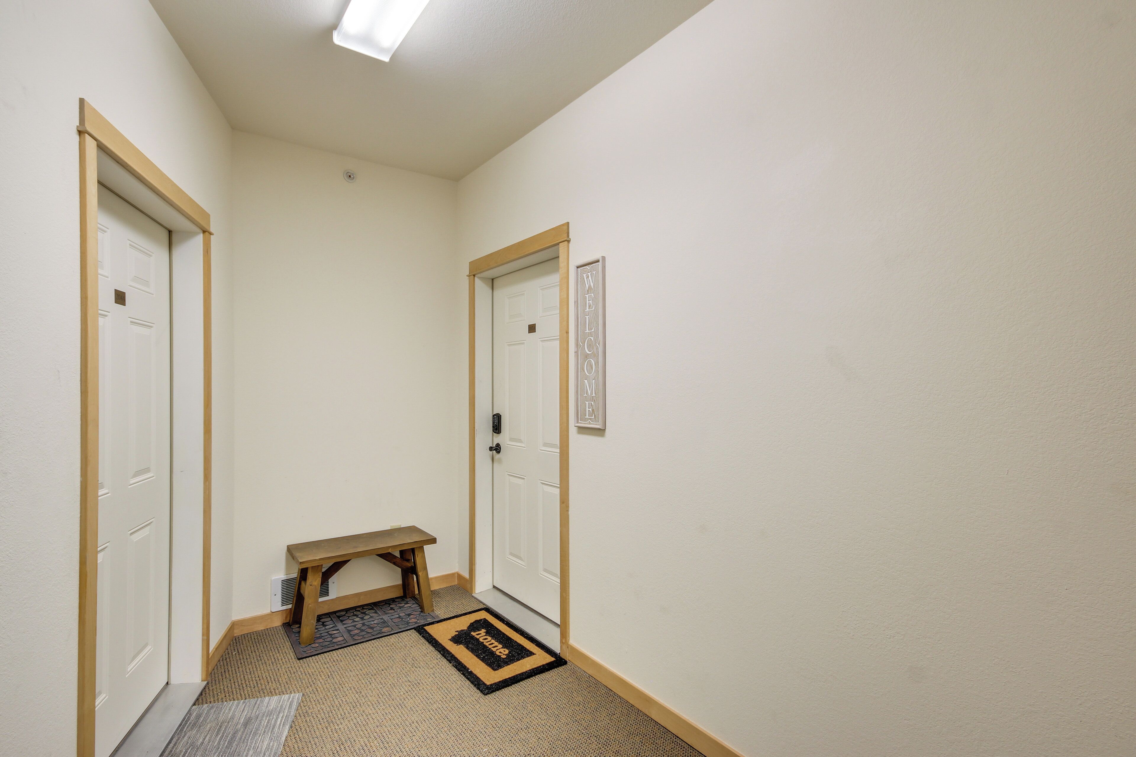 A narrow hallway with two white doors, a wooden bench, and a welcome mat.
