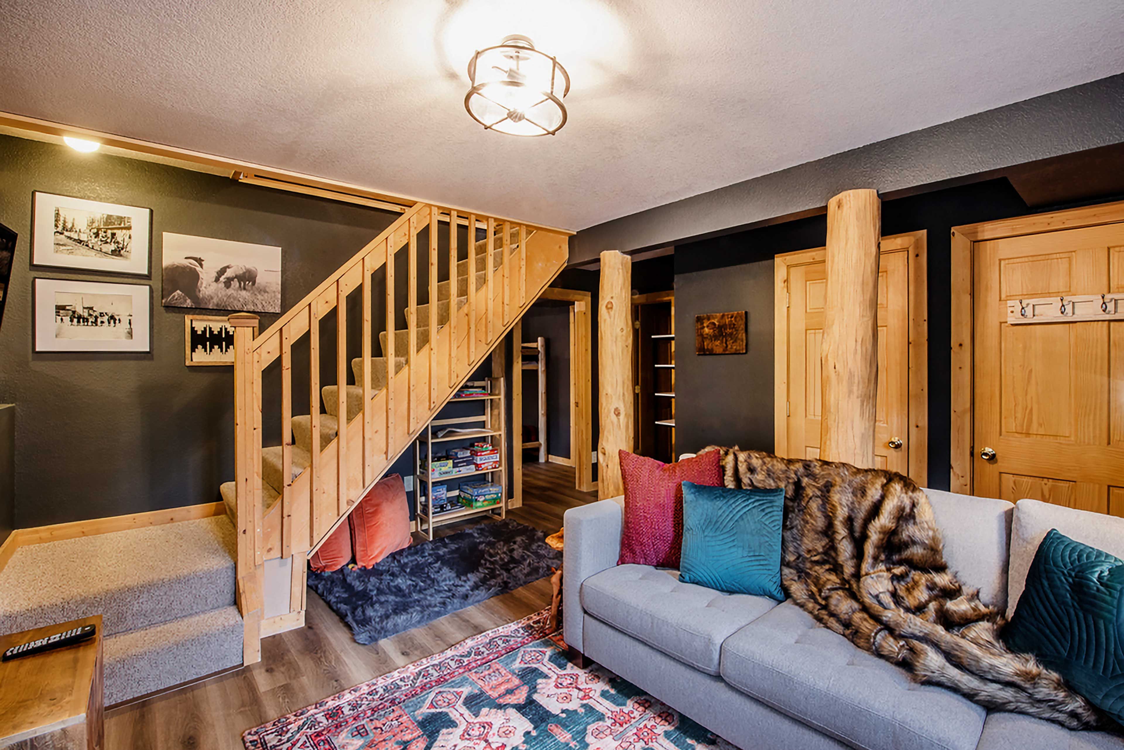 A cozy living room with a grey sofa, a wooden staircase, and a rug.