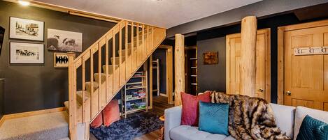 A cozy living room with a grey sofa, a wooden staircase, and a rug.