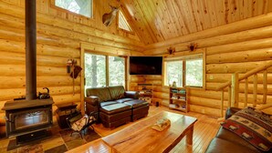 A log cabin interior with a fireplace, leather sofa, wooden table, and a staircase.