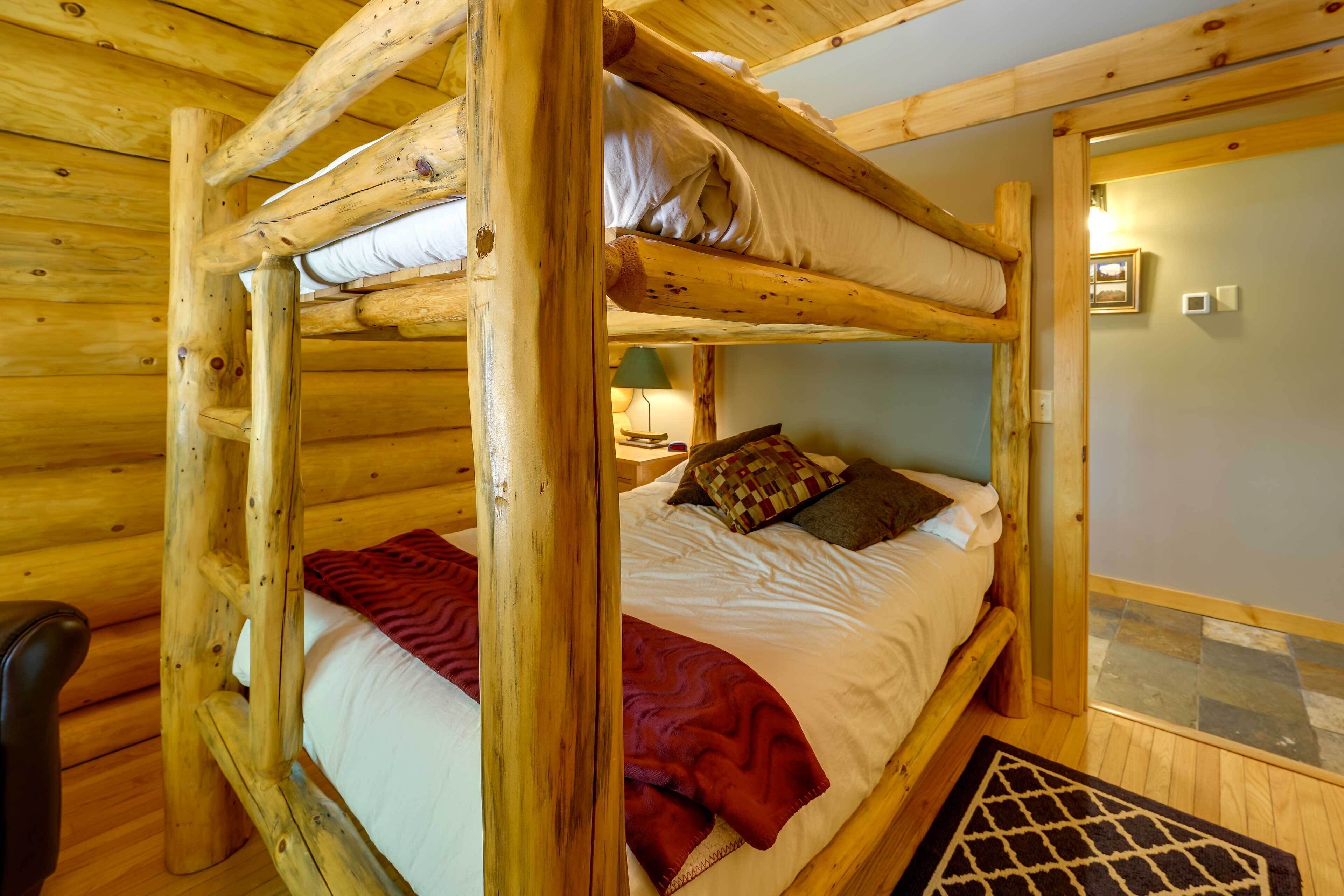 A bunk bed with a red blanket and pillows, wooden walls, and a small table with a lamp.