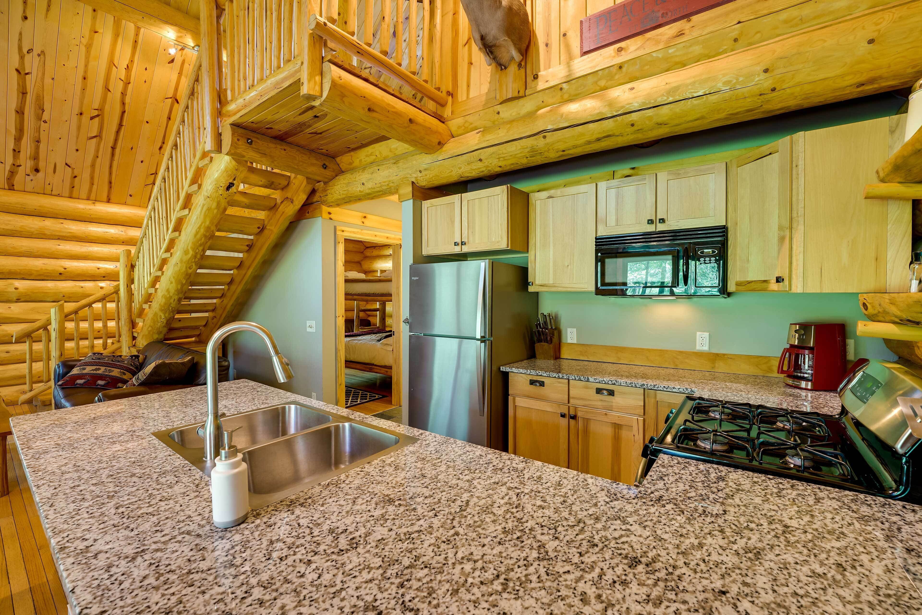 A log cabin interior with a granite countertop, stainless steel appliances, and wooden cabinets.