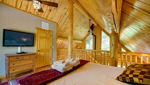 A wooden cabin bedroom with a bed, a TV, a wooden dresser, and a ceiling fan.