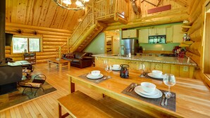 A spacious log cabin interior with a dining area, kitchen, and a loft bedroom.