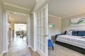 A room with a bed, a chair, a painting, and a door leading to another room. - Graham Home w/ Private Pool & Ping-pong Table! (Graham)