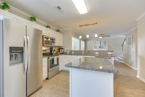 A modern kitchen with stainless steel appliances, a granite countertop island, and white cabinetry. - Graham Home w/ Private Pool & Ping-pong Table! (Graham)