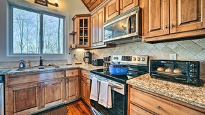 A kitchen with wooden cabinets, a microwave, a stove, a toaster, and a large window. - Glenville Serenity Lodge' w/ Lake Views! (Glenville)