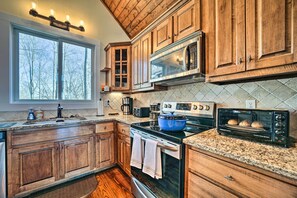 Cucina con mobili in legno, forno a microonde, piano cottura, tostapane e un'ampia finestra.