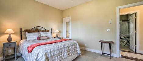 Une chambre à coucher avec un lit, des lampes de chevet, une petite table et une porte donnant sur une autre pièce.
