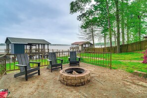 A backyard with a fire pit, two Adirondack chairs, a wooden deck, and a view of a lake. - Waterfront House on Toledo Bend w/ Private Dock! (Many)