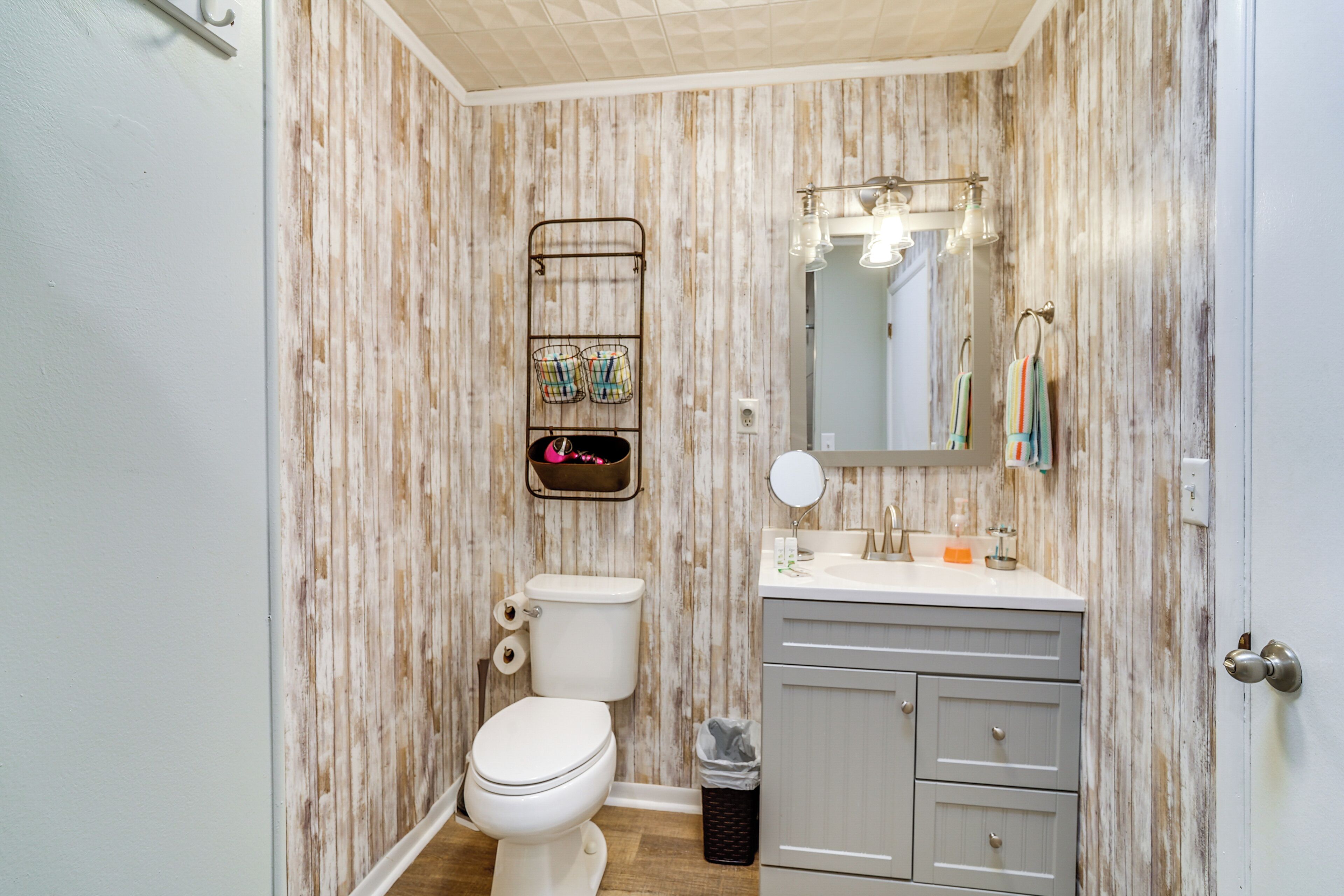 A bathroom with a wooden wall design, a toilet, a sink with a mirror, and a towel rack.