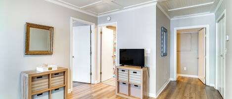 A hallway with wooden flooring, a television on a stand, and a mirror on the wall.