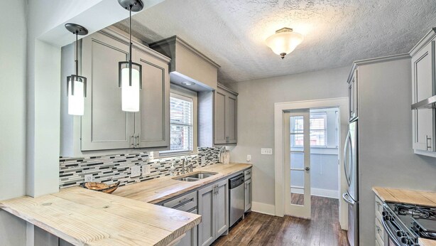 A modern kitchen with grey cabinets, a wooden countertop, a built-in dishwasher, and a stainless steel stove.