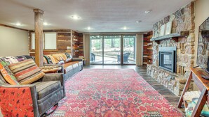 A spacious living room with a stone fireplace, a large window, and a red patterned rug.