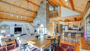 A spacious living area with a stone fireplace, wooden ceiling beams, and a dining area with a red patterned rug. - 'luna Stella' - West Dover Home 1 Mi to Mt Snow! (West Dover)