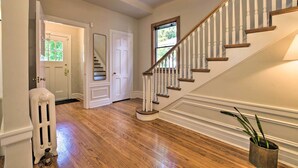 A hallway with a wooden floor, a white radiator, a white door, and a staircase with white balusters and wooden steps. - Classic Oak Park Home, 11 Mi to Downtown Chicago! (Oak Park)