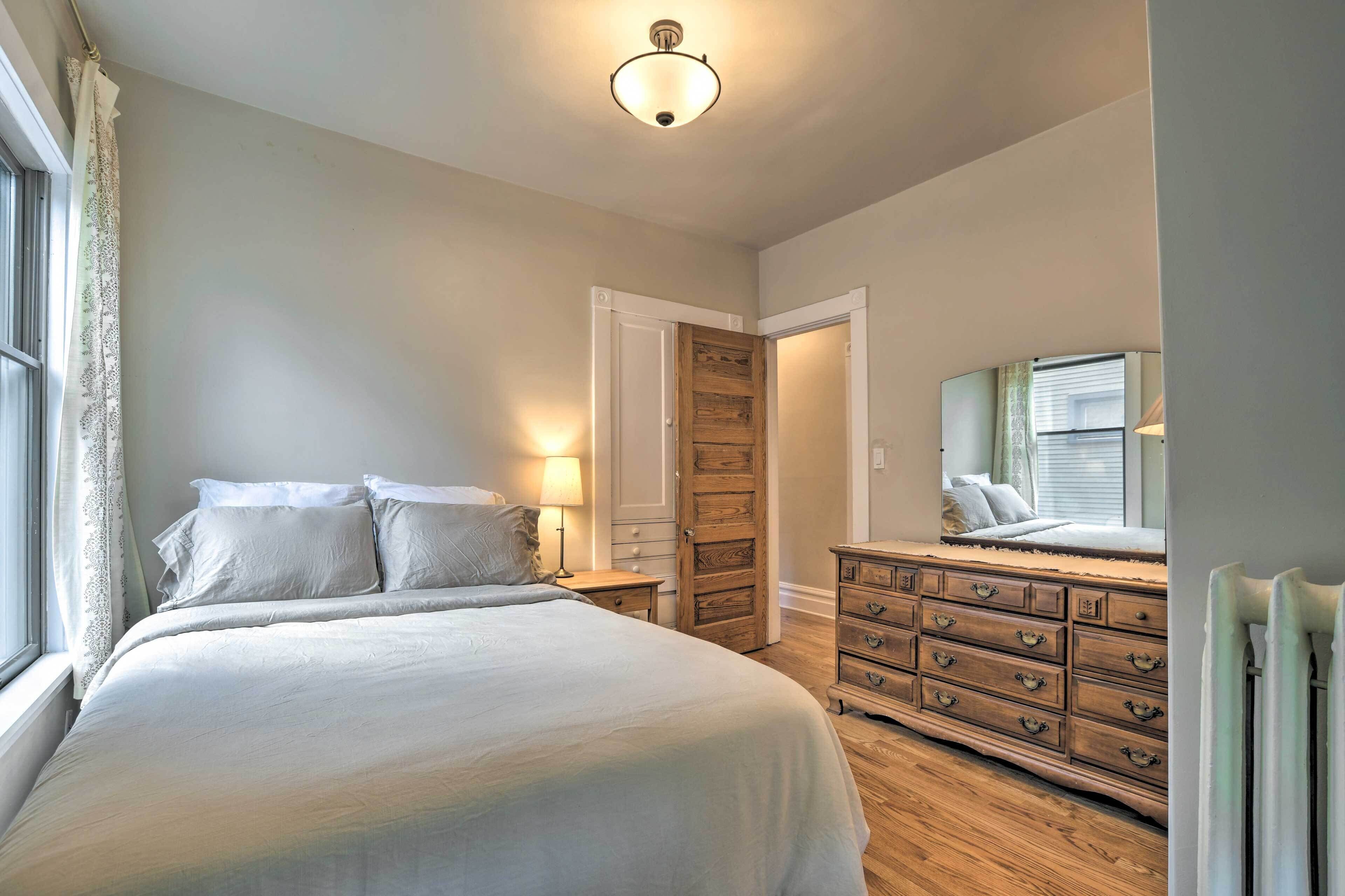 A bedroom with a large bed, a wooden dresser, a nightstand, and a mirror.