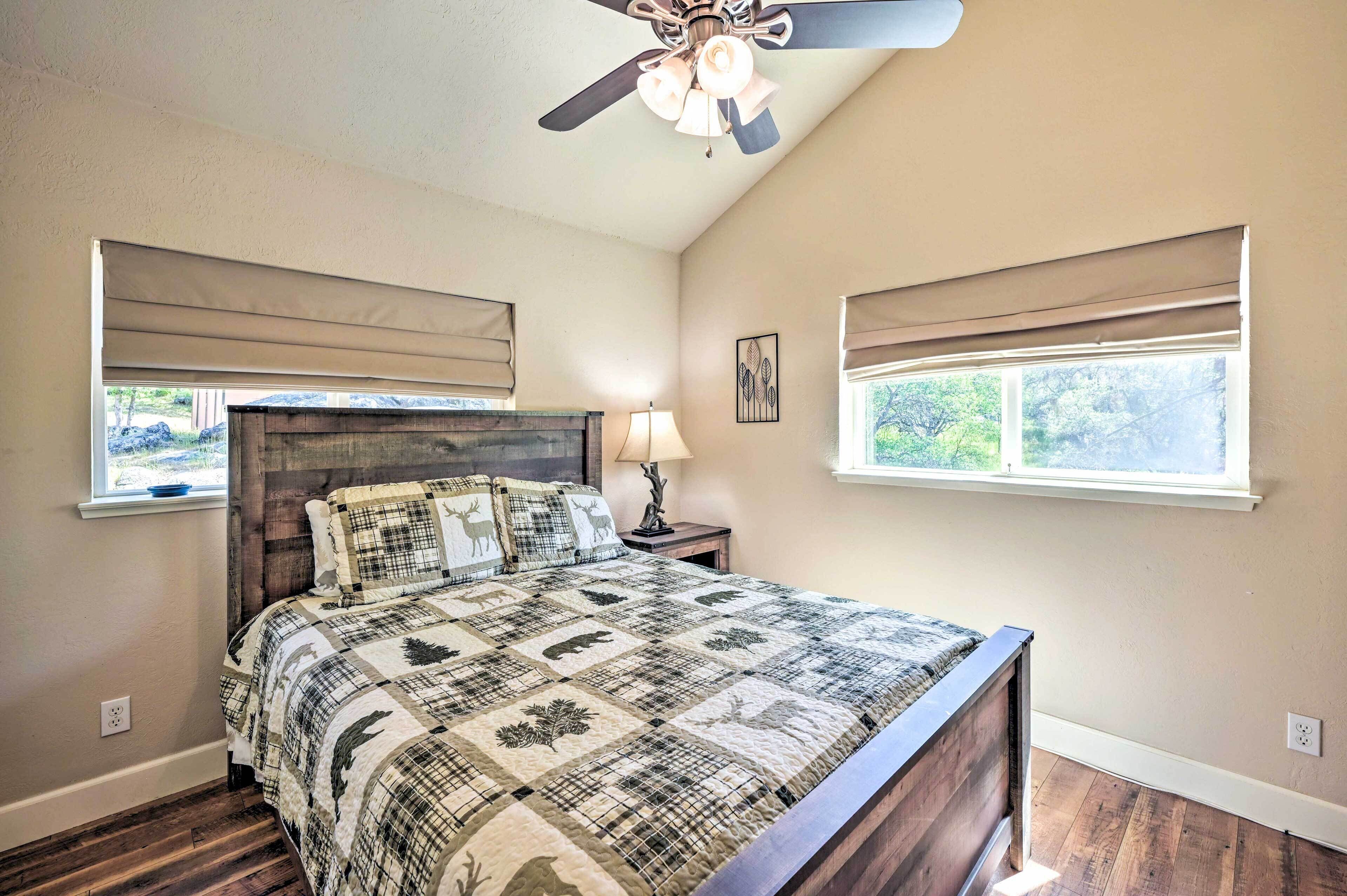 A bedroom with a wooden headboard, a quilted bedspread, a ceiling fan, and two windows with blinds.