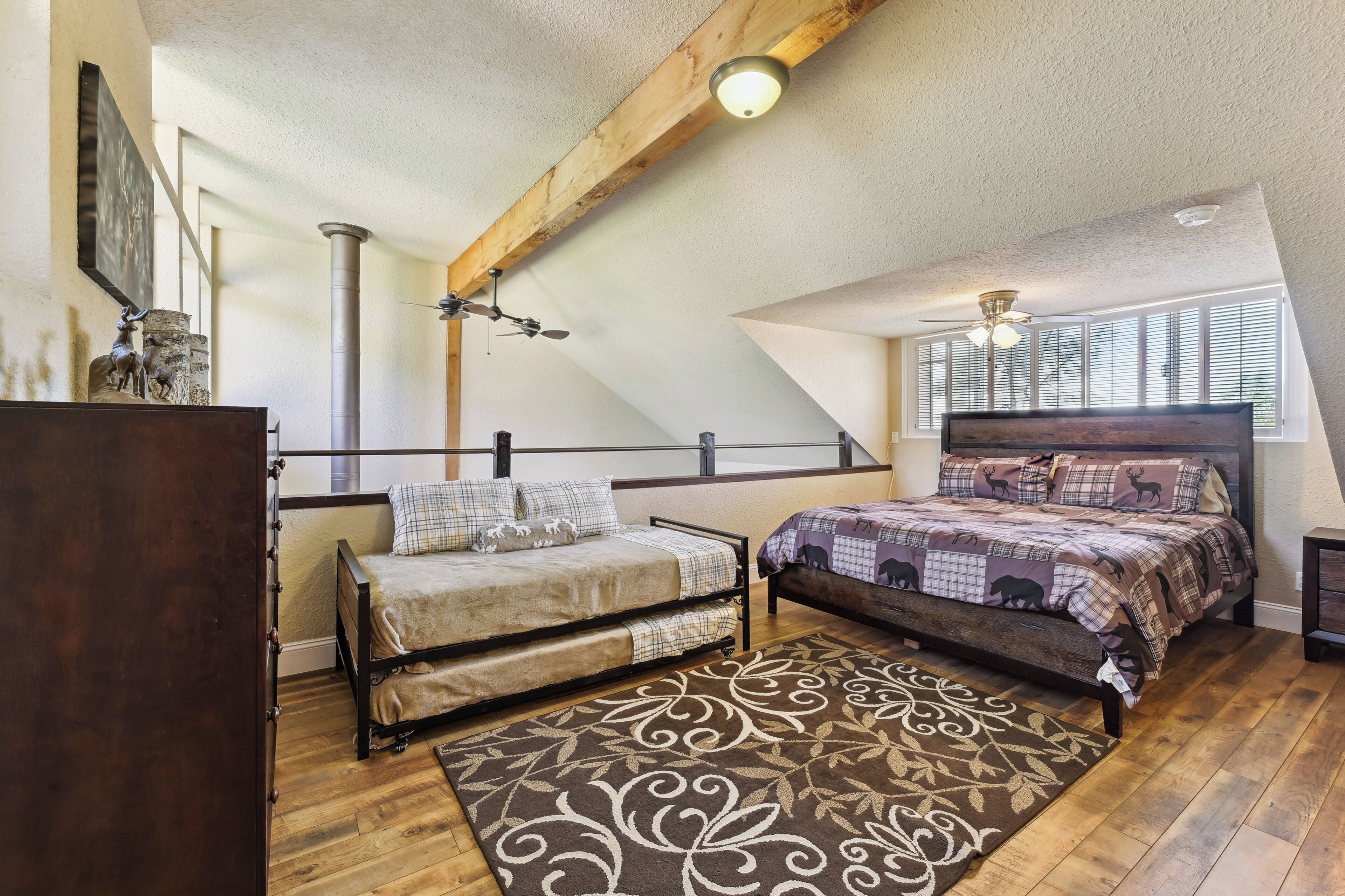 Een slaapkamer met een loft-stijl plafond, een bed met een geborduurde spreideken, een houten vloer en een decoratief vloerkleed.