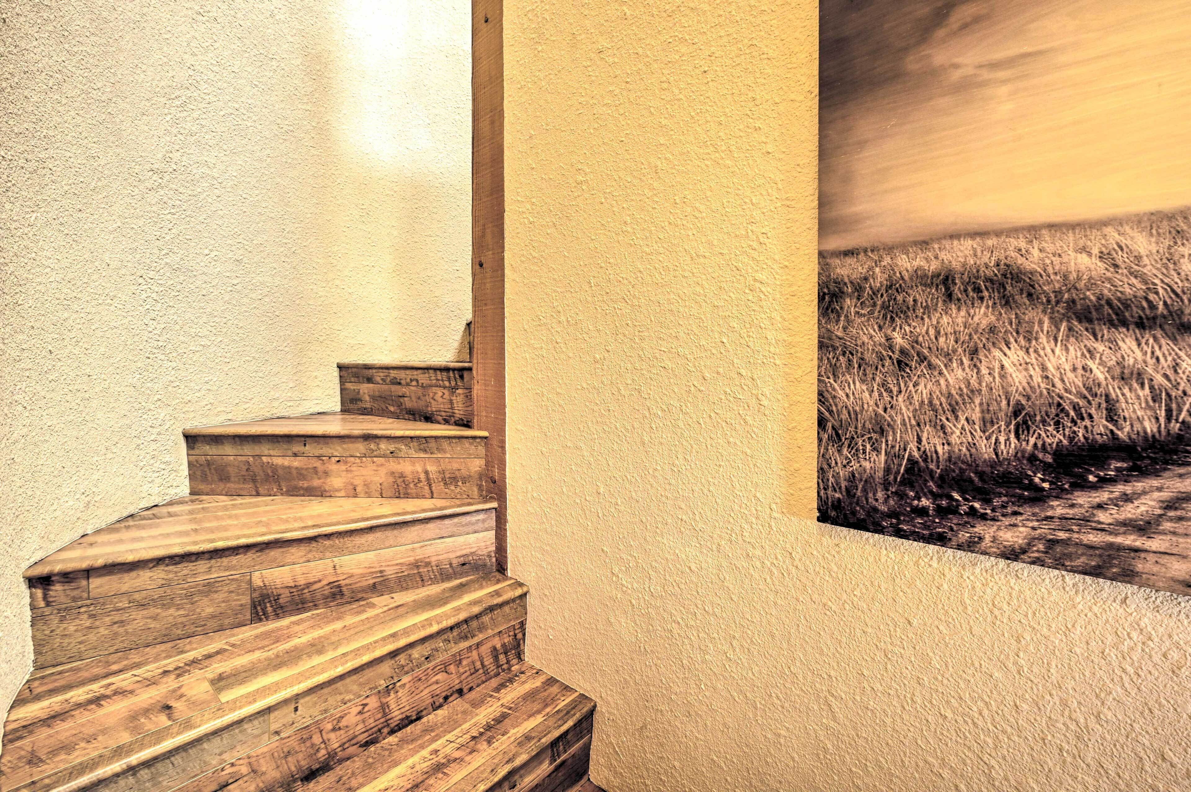 A wooden staircase leading to a room with a textured wall and a painting of a field.