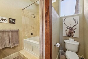 Et badeværelse med badekar, toilet og brusebad. Der er håndklæder på en bøjle, og et billede af et dyr på væggen.