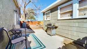 Un patio trasero con una parrilla, muebles de jardín y un árbol.