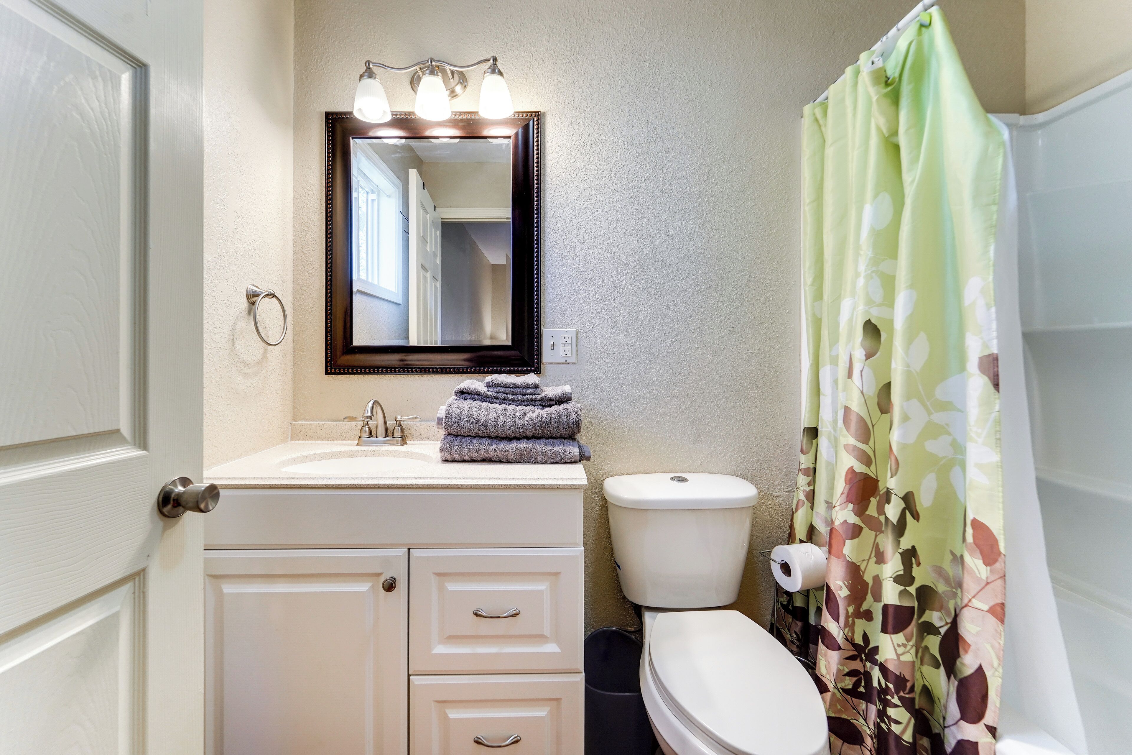 A bathroom with a white sink, a mirror with lights, a toilet, and a shower curtain.