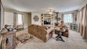 A cozy living room with a brown sofa, a coffee table, and a TV. There are shelves with decorative items and a ceiling fan. - Ruidoso Home w/ Patio, Walk to Restaurants! (Ruidoso)
