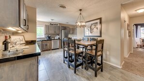 A modern kitchen with dark wooden chairs, a central island, and a chandelier. - Ruidoso Home w/ Patio, Walk to Restaurants! (Ruidoso)