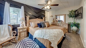 A bedroom with a bed, nightstands, a dresser, a ceiling fan, a window with curtains, and a large potted plant. - Ruidoso Home w/ Patio, Walk to Restaurants! (Ruidoso)