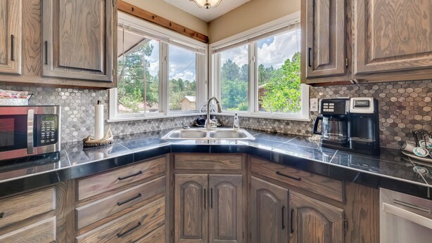 A kitchen with dark wood cabinets, a black countertop, a double sink, and a coffee maker. - Ruidoso Home w/ Patio, Walk to Restaurants! (Ruidoso)