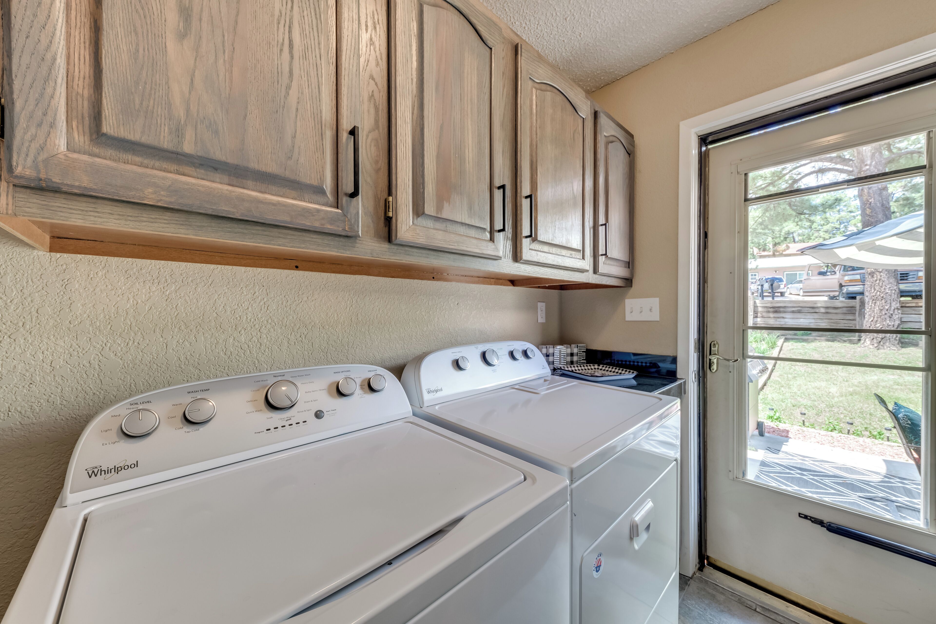 A laundry room with two Whirlpool washers and wooden cabinets above.